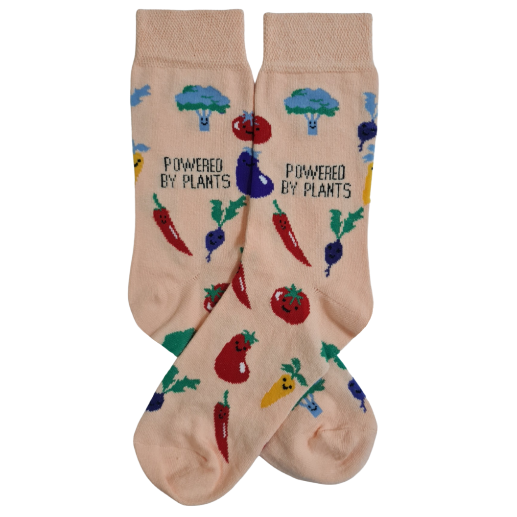 A pair of beige socks with a colorful vegetable design and the text 'Powered By Plants' on the cuff.