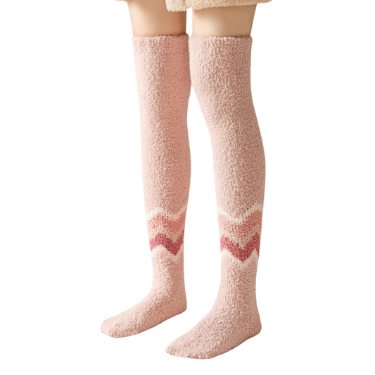 Person wearing a pair of soft pink fluffy thigh-high socks featuring a subtle chevron zigzag pattern across the calves in alternating shades of pink.