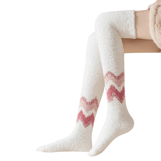 Person wearing a pair of soft white fluffy thigh-high socks featuring a pink and red chevron zigzag pattern across the calves.