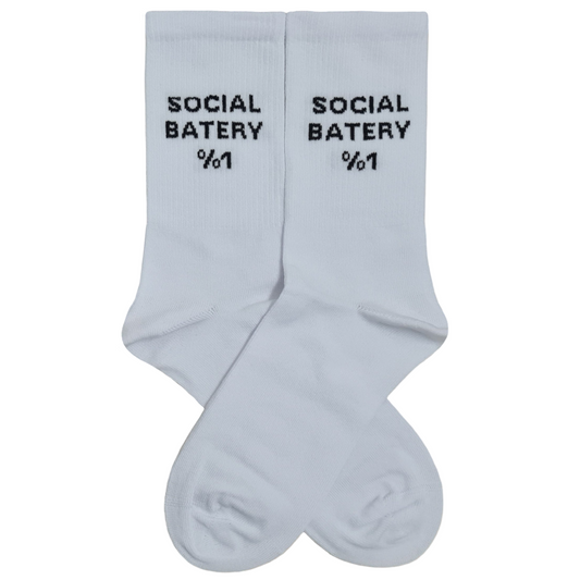 A pair of white crew socks displayed flat against a white background, featuring the black knitted text "SOCIAL BATERY %1" below the ribbed cuffs.