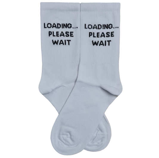 A pair of white mid-calf crew socks displayed flat, featuring the text "LOADING... PLEASE WAIT" embroidered in a bold, black pixelated digital font on the upper ribbed leg section.